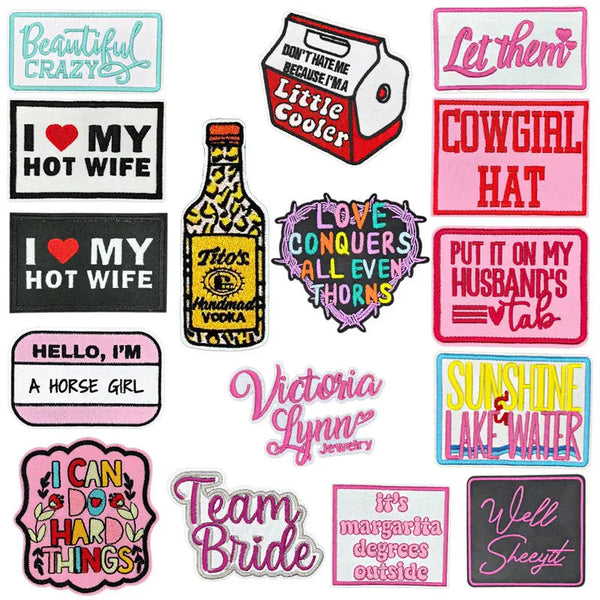 A collection of embroidered iron-on clothing patches featuring various text designs like I love my hot wife and Let them.