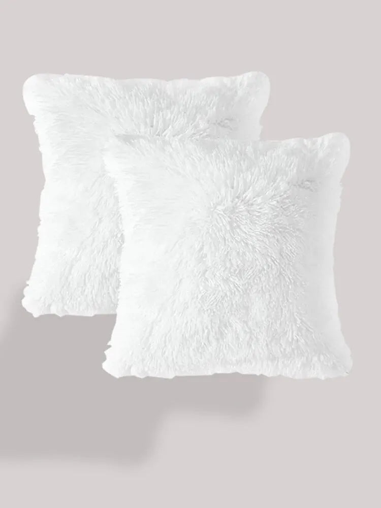 Two fluffy white velvet throw pillows stacked against a light gray background.