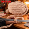 A hand is measuring a large ball of light pink chunky chenille yarn on a wooden table.