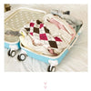 A light blue travel organizer storage set with a lid is shown open, filled with folded clothing and accessories on a white be
