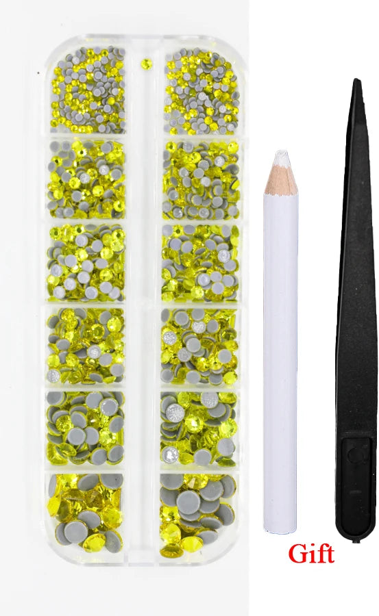 A clear plastic container holds various yellow and silver crystal rhinestones and an applicator tool for crafting.
