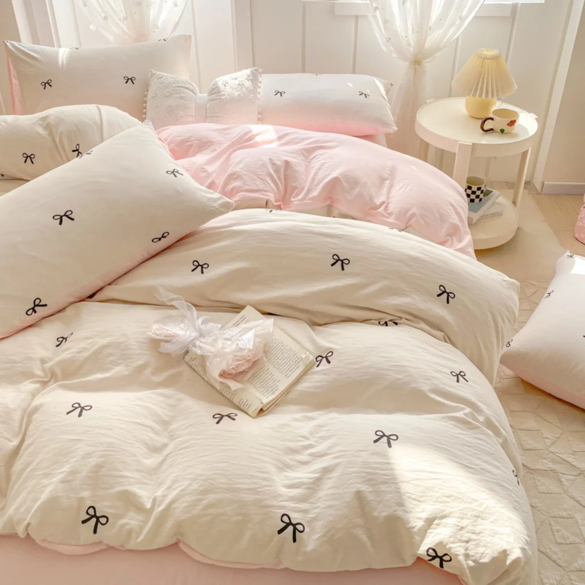A set of three pink and white bedding pieces featuring bowknot embroidery on a duvet cover and pillows.