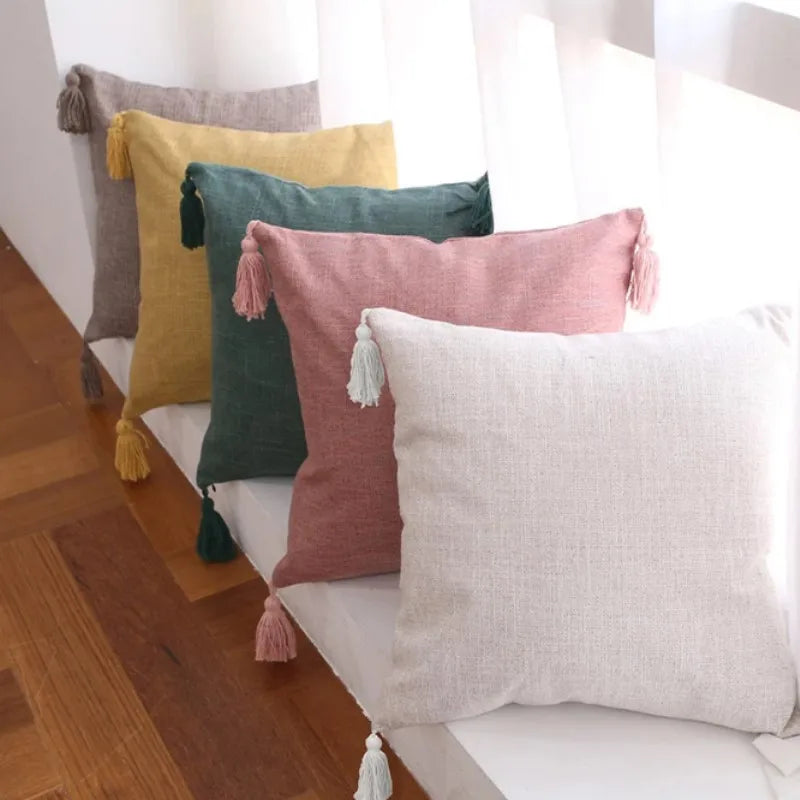 A collection of boho cotton linen throw pillow covers in shades of yellow, olive green, pink, and beige arranged on a white s