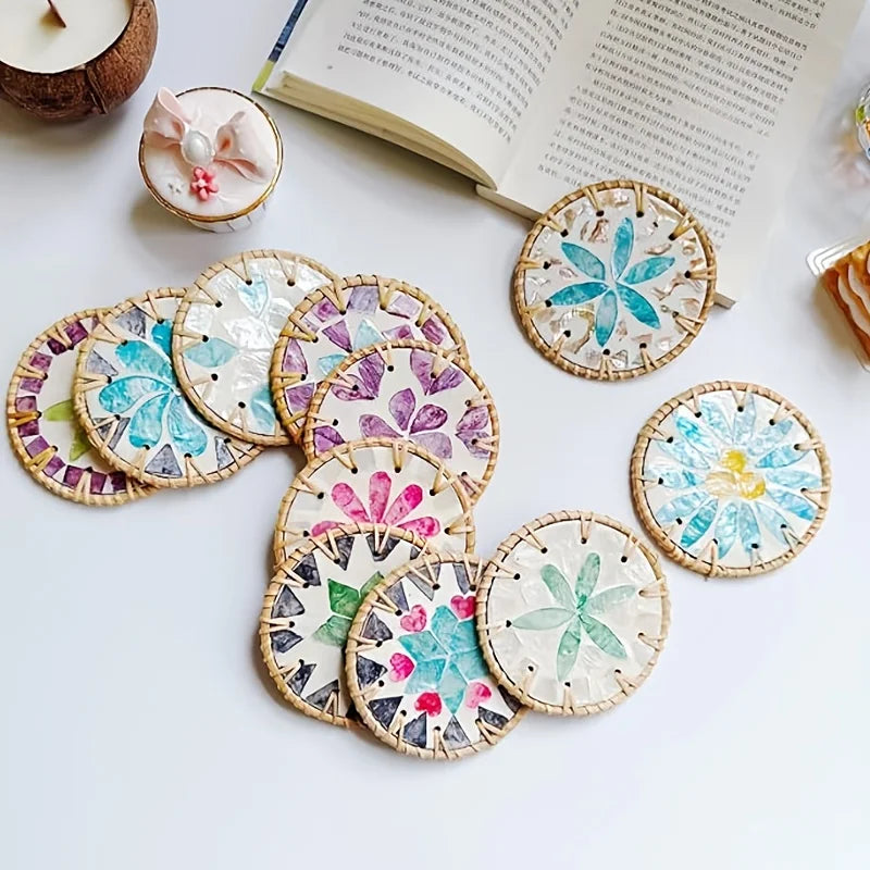 A set of five woven shell coasters featuring various floral and geometric patterns on a white surface.