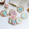 A set of five woven shell coasters featuring various floral and geometric patterns on a white surface.