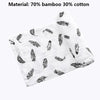A white muslin swaddle blanket featuring a pattern of feather and leaf designs made from 70% bamboo and 30% cotton.