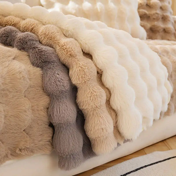 A stack of plush rabbit fur sofa cushion covers in shades of beige, cream, and gray.