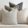 A grouping of four textured pillows in shades of gray and beige on a light sofa.
