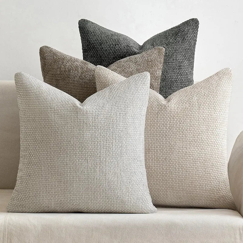 A grouping of four textured pillows in shades of gray and beige on a light sofa.