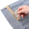 A hand is applying self-adhesive beige hem tape to the edge of blue denim fabric.