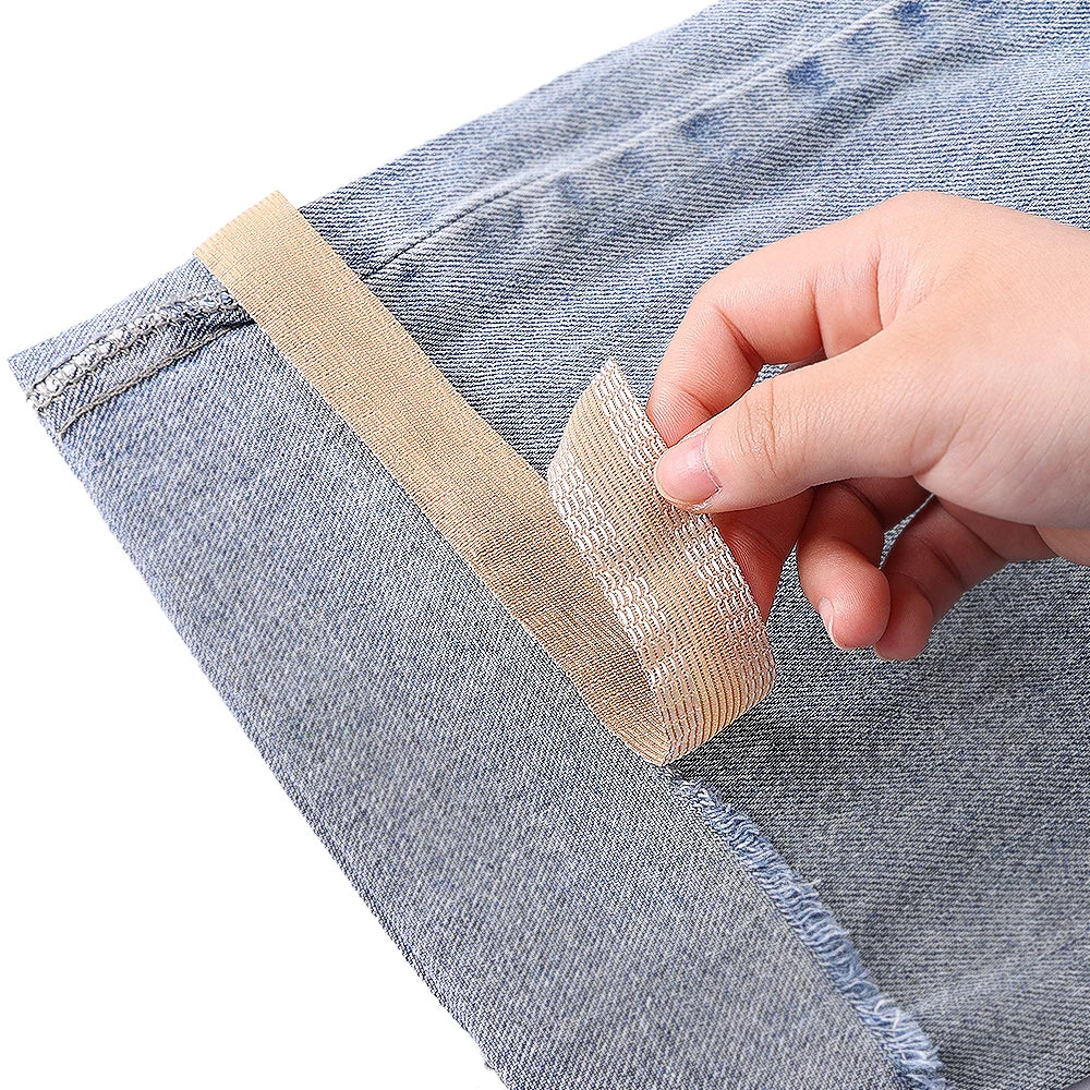 A hand is applying self-adhesive beige hem tape to the edge of blue denim fabric.