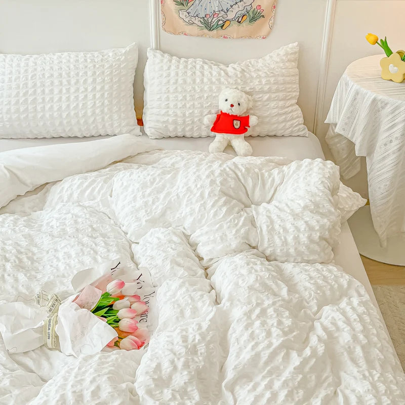 A white quilted duvet cover set with a sheep plush toy and pink flowers on a bed.