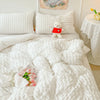 A white quilted duvet cover and pillow set with a small white teddy bear and pink flowers on a bed.