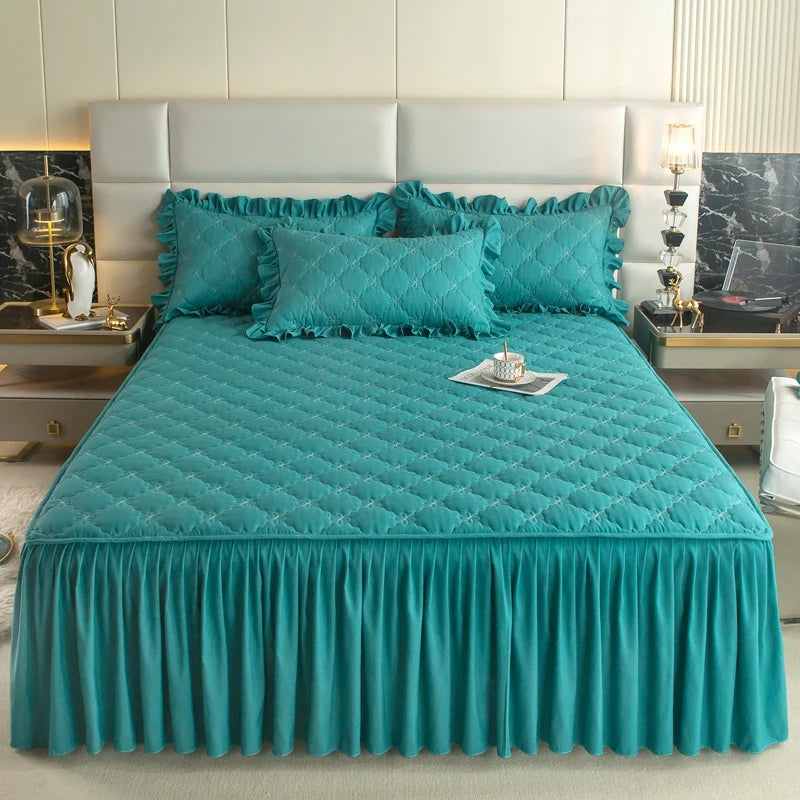A teal quilted bed skirt cover displayed on a bed with a white upholstered headboard and bedside tables.