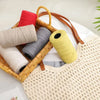 A collection of hand-woven cotton yarn in red, gray, and yellow is displayed in a wooden basket on a white surface.