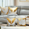 Decorative throw pillows featuring white feathers with gold accents on a gray sofa.