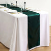 A white tablecloth with a dark green satin table runner, silverware, and glassware set for an elegant dining table.