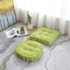 A bright lime green tufted corduroy floor seat cushion resting on a light gray patterned rug near a window.