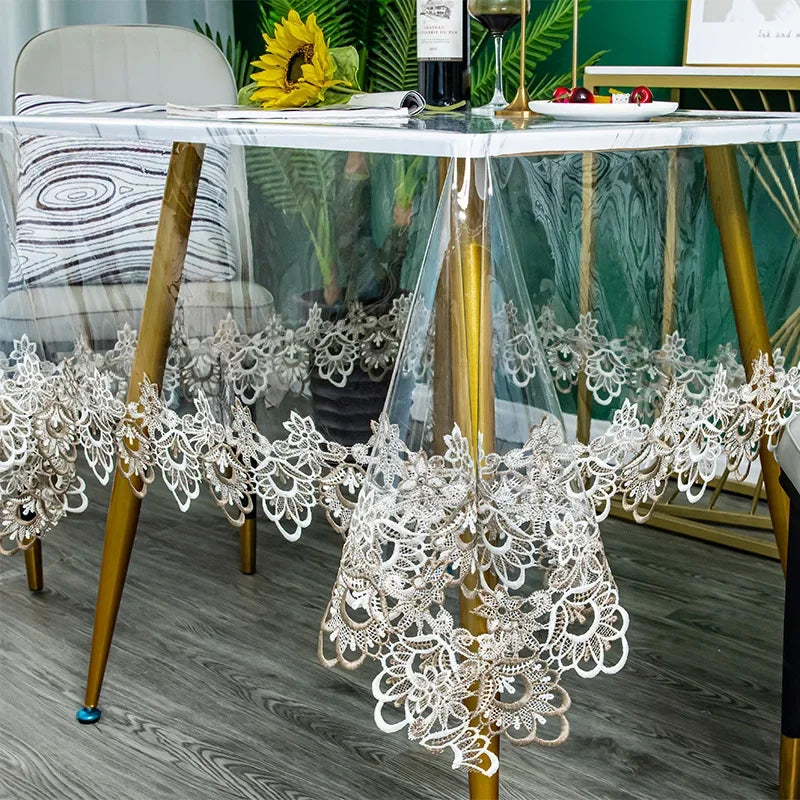 A clear glass table is decorated with white lace embroidery and floral accents on a wooden surface.
