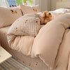 A beige and brown cartoon embroidered bedding set featuring pillows and a duvet on a bed.