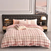 A pink plush rabbit hair bedding set with a quilted duvet and pillows displayed on a dark upholstered bed.