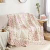 A pink and cream patchwork floral plaid cotton quilt draped over a sofa.