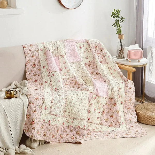 A pink and cream patchwork floral plaid cotton quilt draped over a sofa.