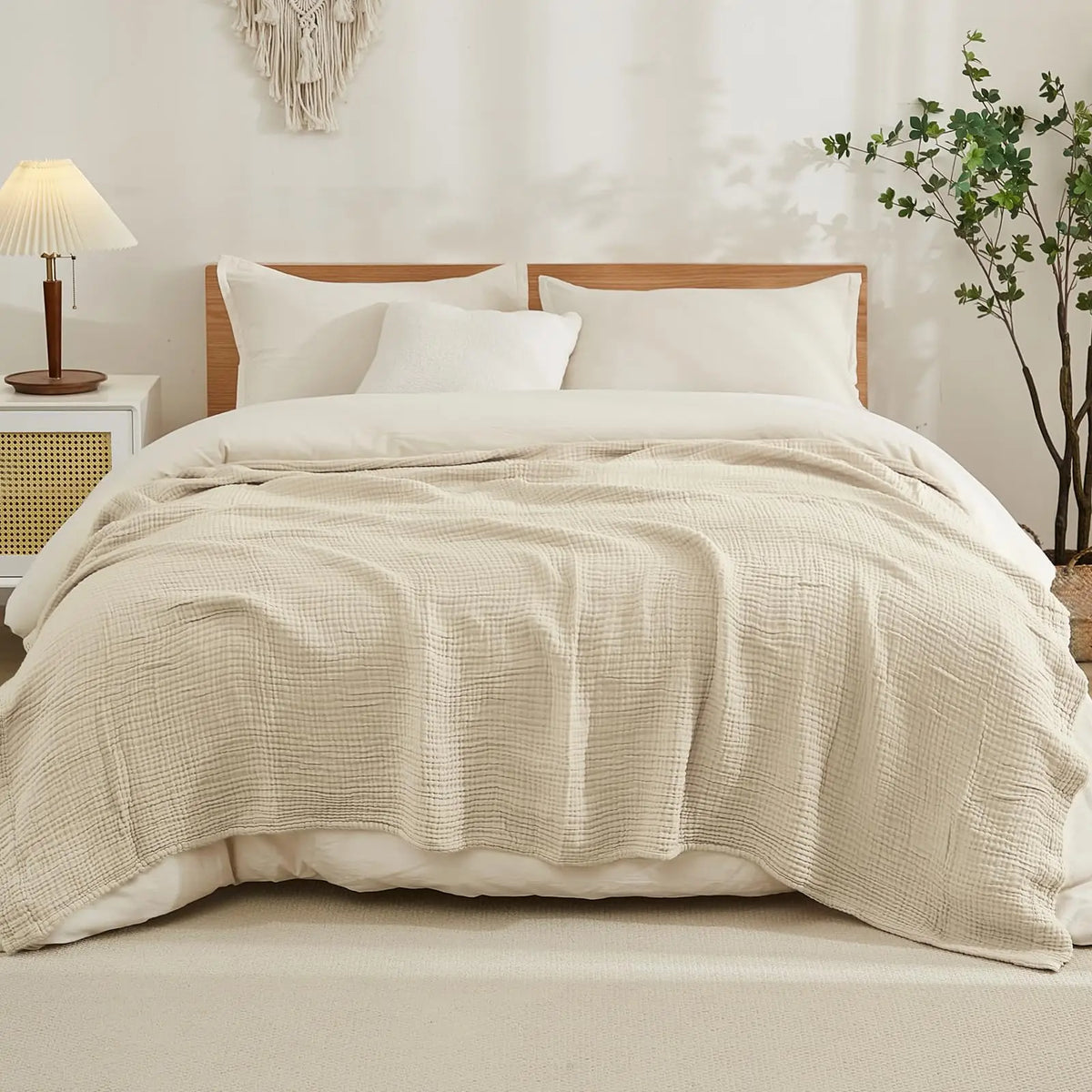A beige quilted blanket is draped over a white duvet on a bed with a wooden headboard and natural light.