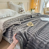 A thick gray knitted blanket is draped over a bed, featuring vertical ribbed texture and a small teacup on the surface.