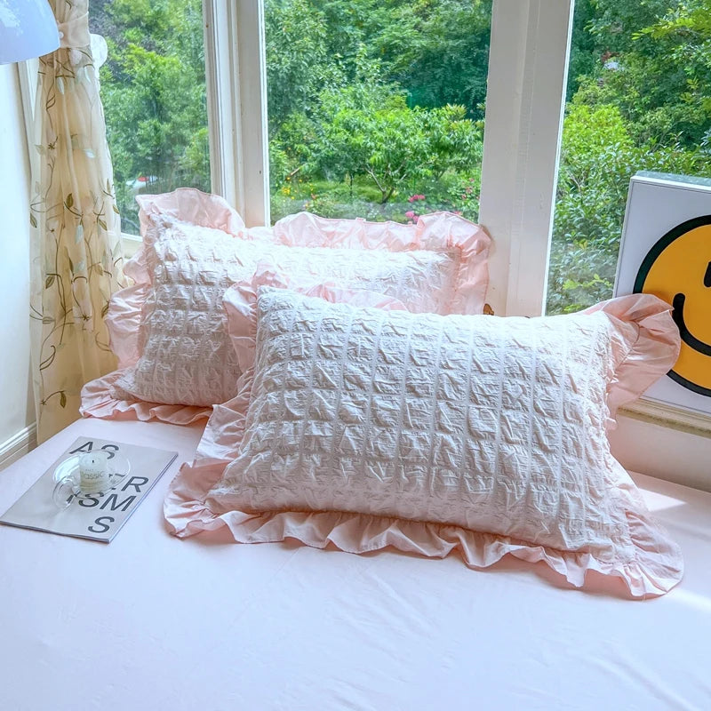 A set of pink lace seersucker pillows with ruffled edges displayed on a white bed.