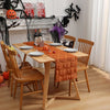 A wooden dining table set for a festive Halloween meal with an orange runner and spooky decorations.