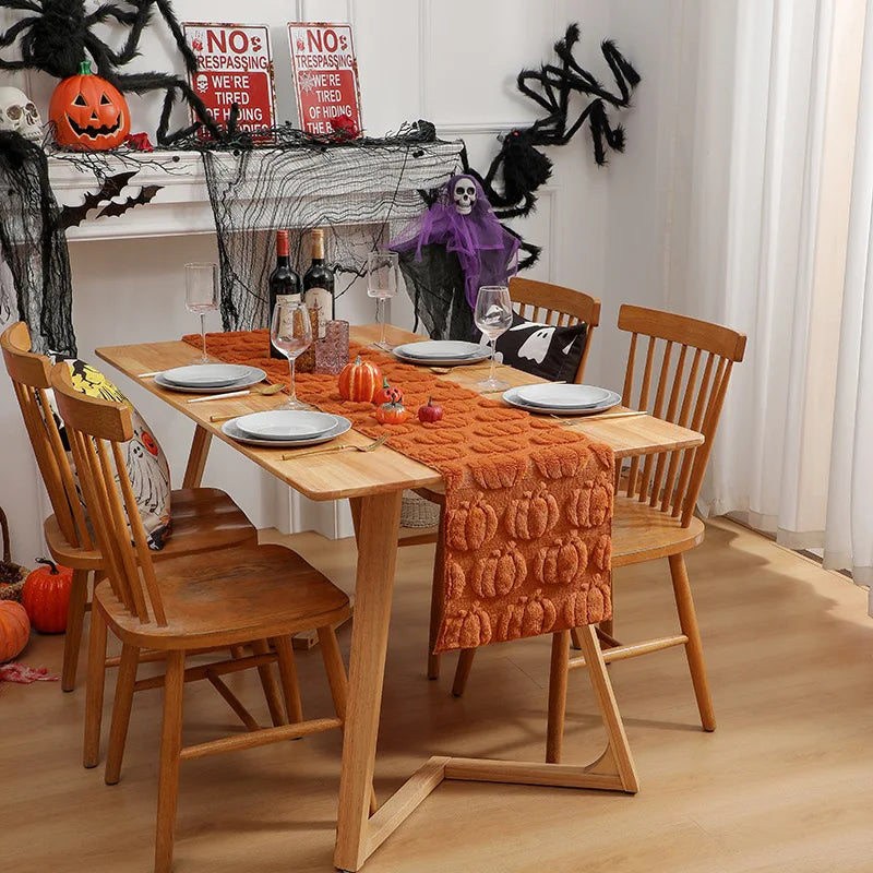 A wooden dining table set for a festive Halloween meal with an orange runner and spooky decorations.