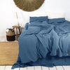 A deep blue luxury French linen duvet cover draped on a bed with natural textures and a straw light fixture above.