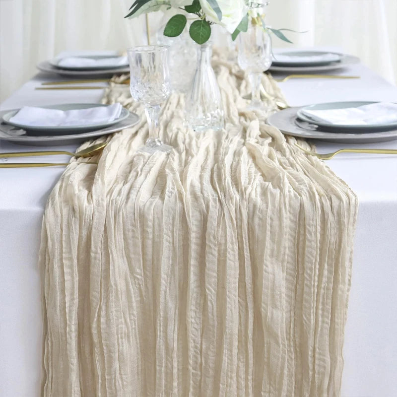 A cream semi-sheer gauze table runner draped over a white tablecloth with silver plates and glassware.