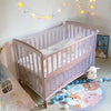 A light pink portable mosquito net for cribs is displayed in a nursery setting with string lights and soft toys.