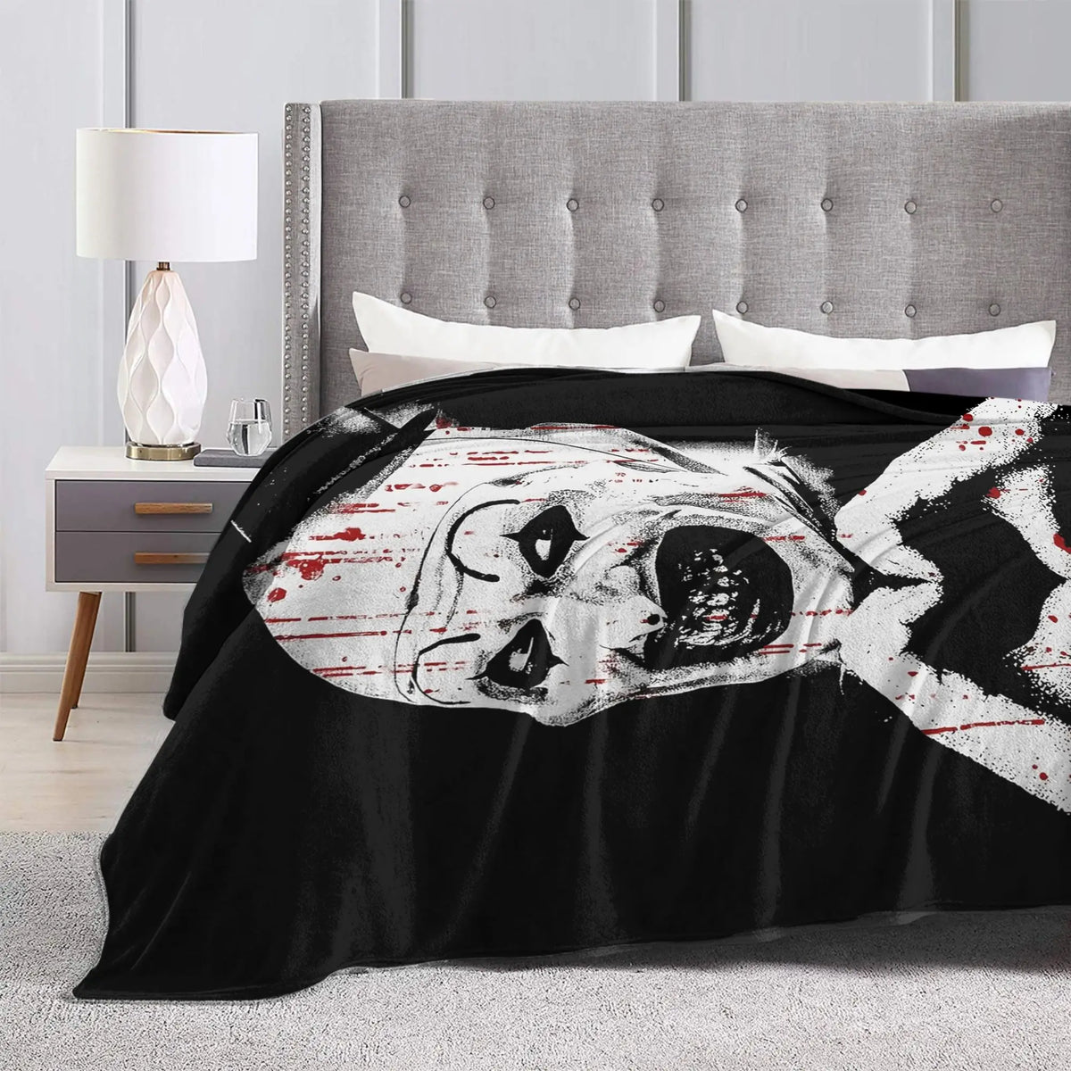 A black throw blanket featuring a distressed white face design is displayed on a bed.