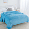 A bright blue coral fleece throw blanket draped over a white bed in a well-lit room.