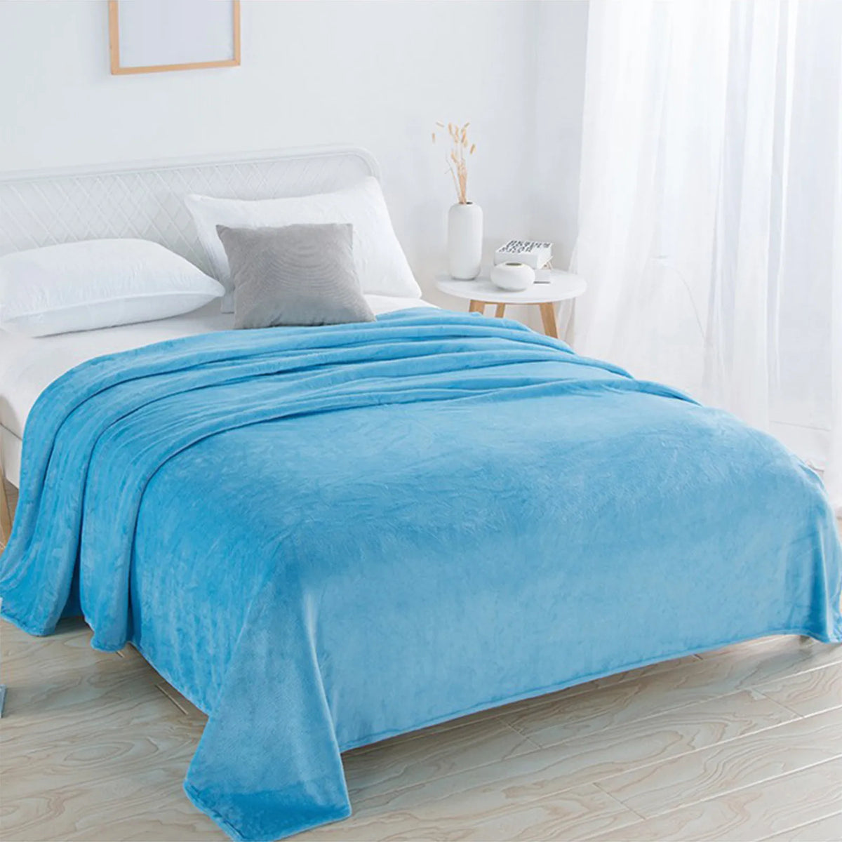 A bright blue coral fleece throw blanket draped over a white bed in a well-lit room.
