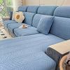 A light blue jacquard stretch sofa cover featuring a wavy texture and cream accent pillows on a modern sofa.
