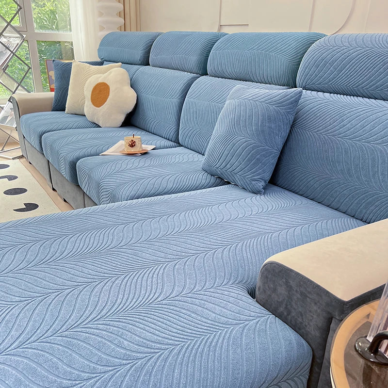 A light blue jacquard stretch sofa cover featuring a wavy texture and cream accent pillows on a modern sofa.