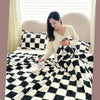 A woman is relaxing on a bed covered with a black and white checkered panda velvet multifunctional blanket.