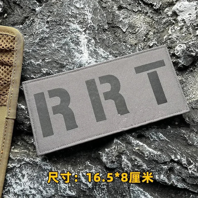 A rectangular gray hook and loop patch labeled RRT is placed on a dark, textured rock surface.