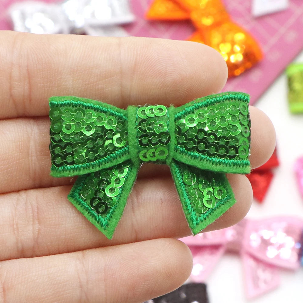A hand holds a bright green sequin bow patch for DIY decoration.