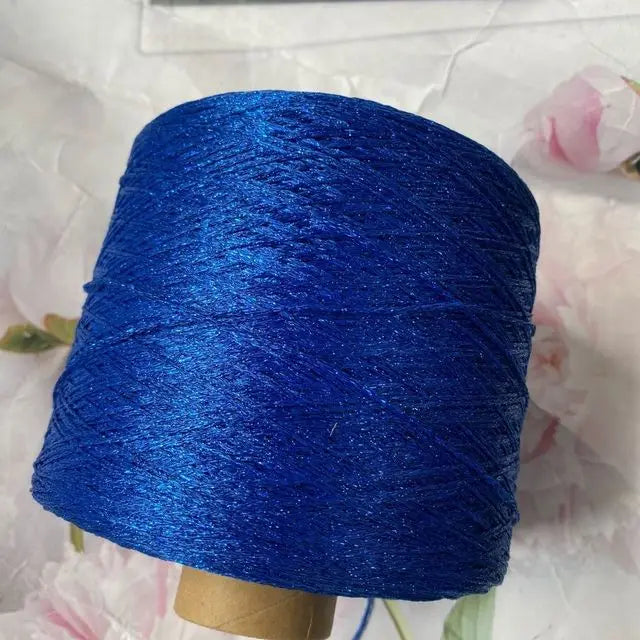 A skein of bright blue glitter metallic yarn is wound around a wooden bobbin for crochet or knitting.