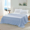 A light blue ice silk cooling blanket is draped over a white bed with white pillows in a bright, airy bedroom.