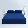 A deep blue ice silk cooling fitted bed sheet set displayed on a bed with matching pillows and a white lamp.