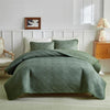 A light green quilted duvet and pillow set on a bed with white paneled walls.