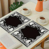 A set of vintage skull placemats featuring a gothic floral mystic cross design placed on a white table.