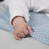 A baby's hand rests on a light blue waffle blanket.