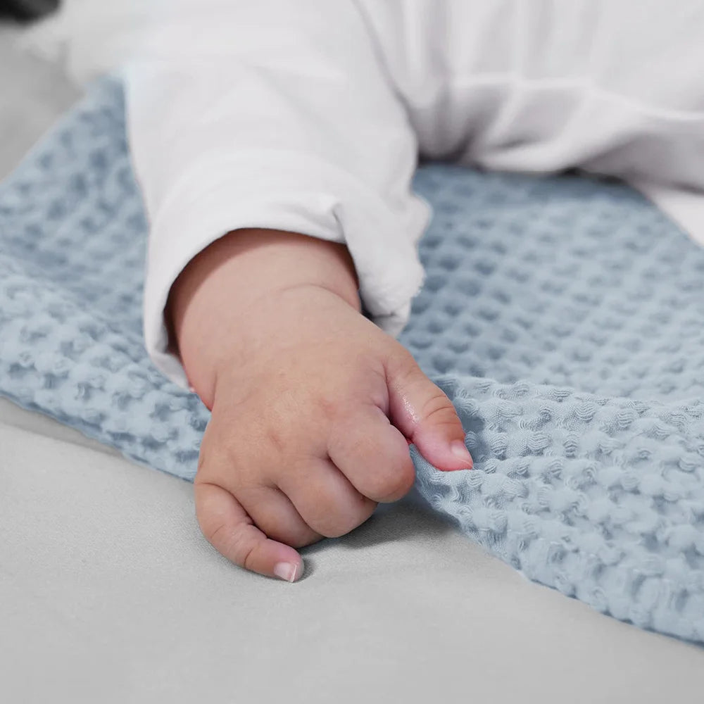 A baby's hand rests on a light blue waffle blanket.